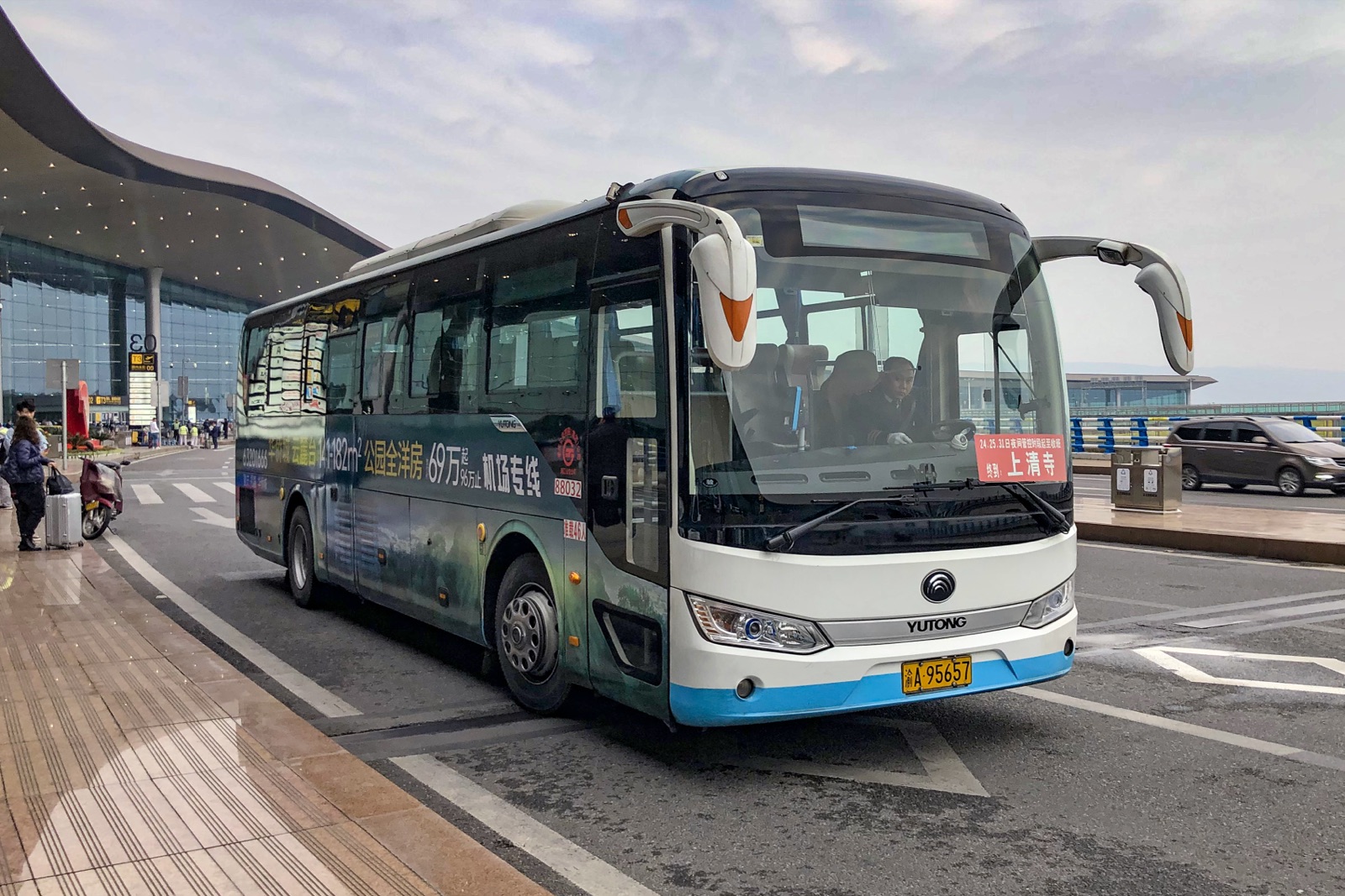 A K01 airport bus at the Terminal 3 curbside, the ¥15 line toward 解放碑.