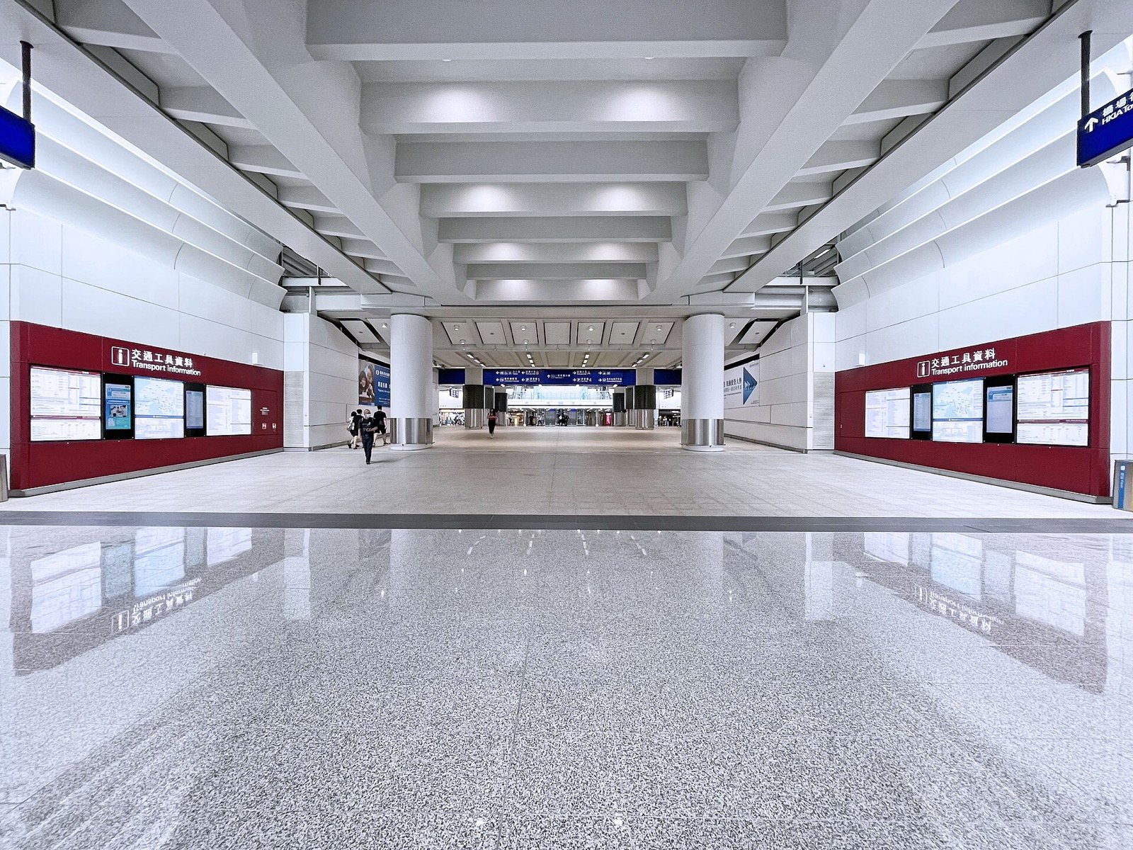 The wide walkway linking Airport Station to Terminal 1, red 'Transport Information' signage on both sides and blue directional signs overhead.