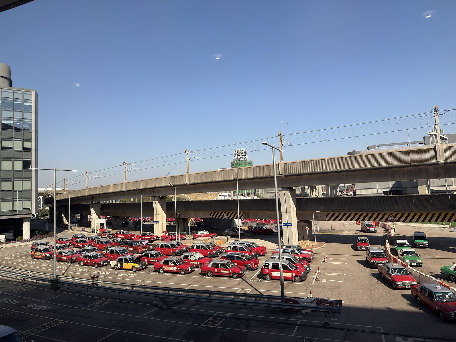 The taxi holding area in daylight, rows of red urban taxis with a line of green New Territories taxis to the right — red for the main urban area, green for the New Territories.