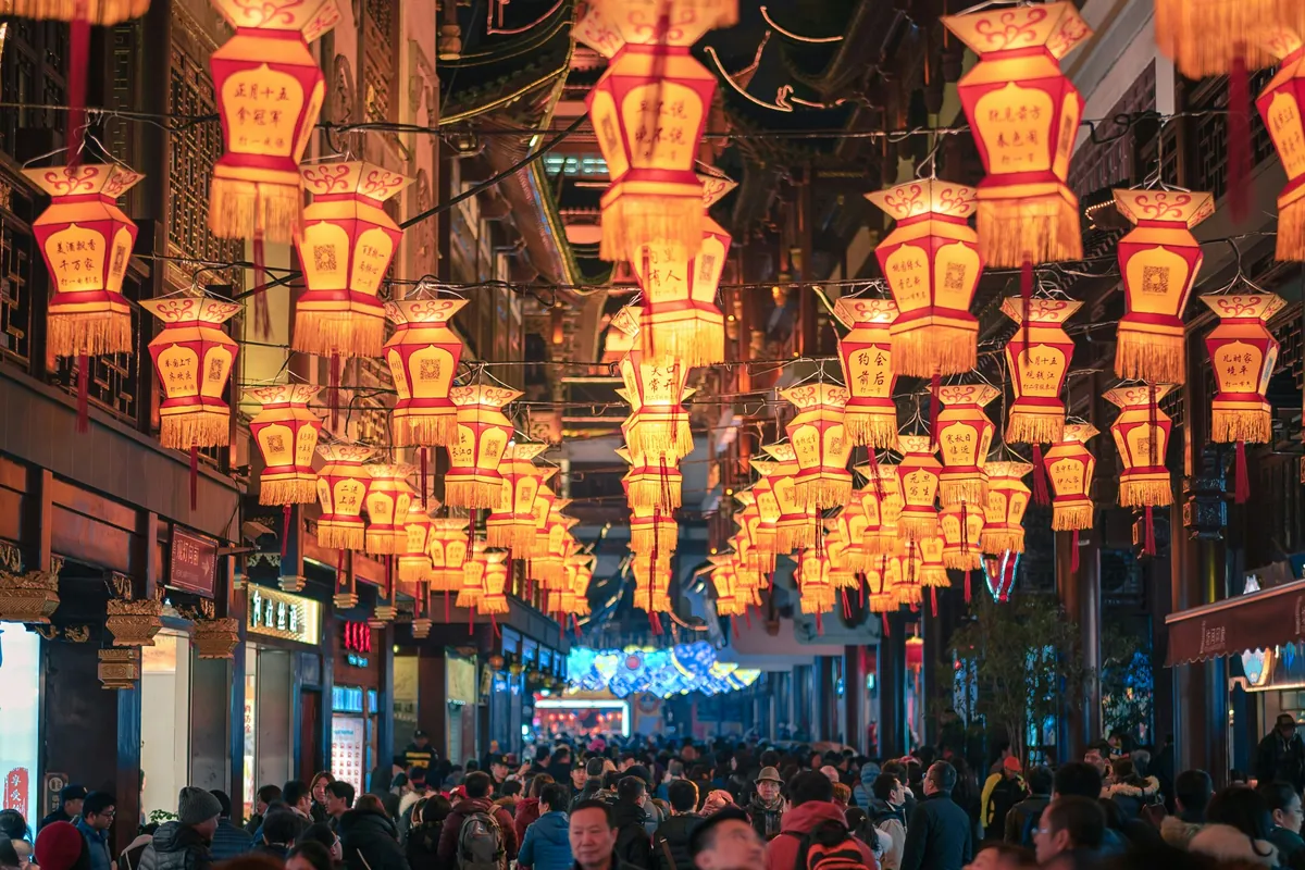 The Yuyuan bazaar district in Shanghai alive with evening crowds — rows of red lanterns hang overhead above traditional shopfronts, the kind of scene where mobile payment is the only practical way to buy anything.