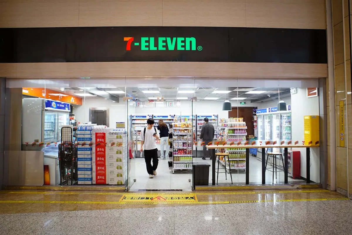 Inside a 7-Eleven convenience store in mainland China — brightly lit aisles stocked with snacks and drinks, a low-stakes environment where travelers discover whether their foreign card or Alipay setup actually works.